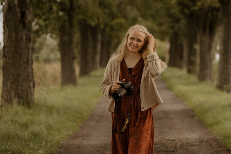 Fotografen Sara i trädallé, ler med kameran i handen.