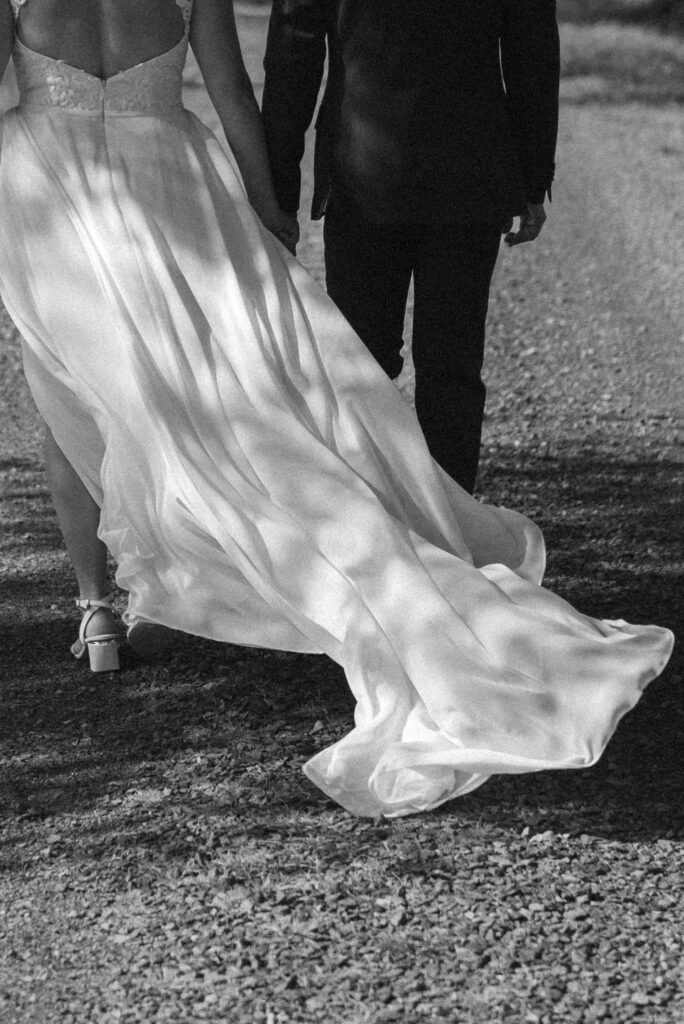 Brudpar går på grusväg under fotograferingen, brudklänningen blåser i vinden.